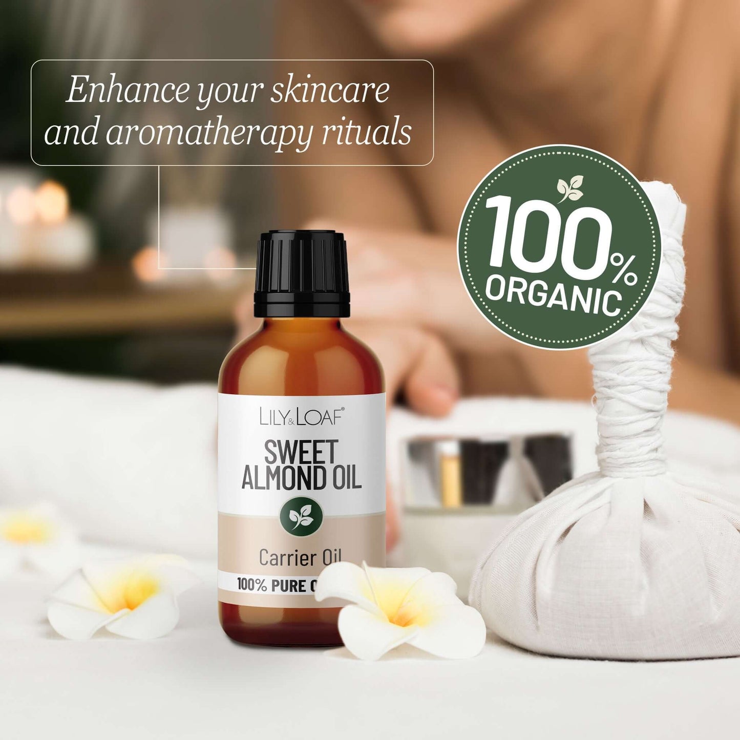 Bottle of sweet almond oil with a 100% organic label, surrounded by flowers and a blurred background.