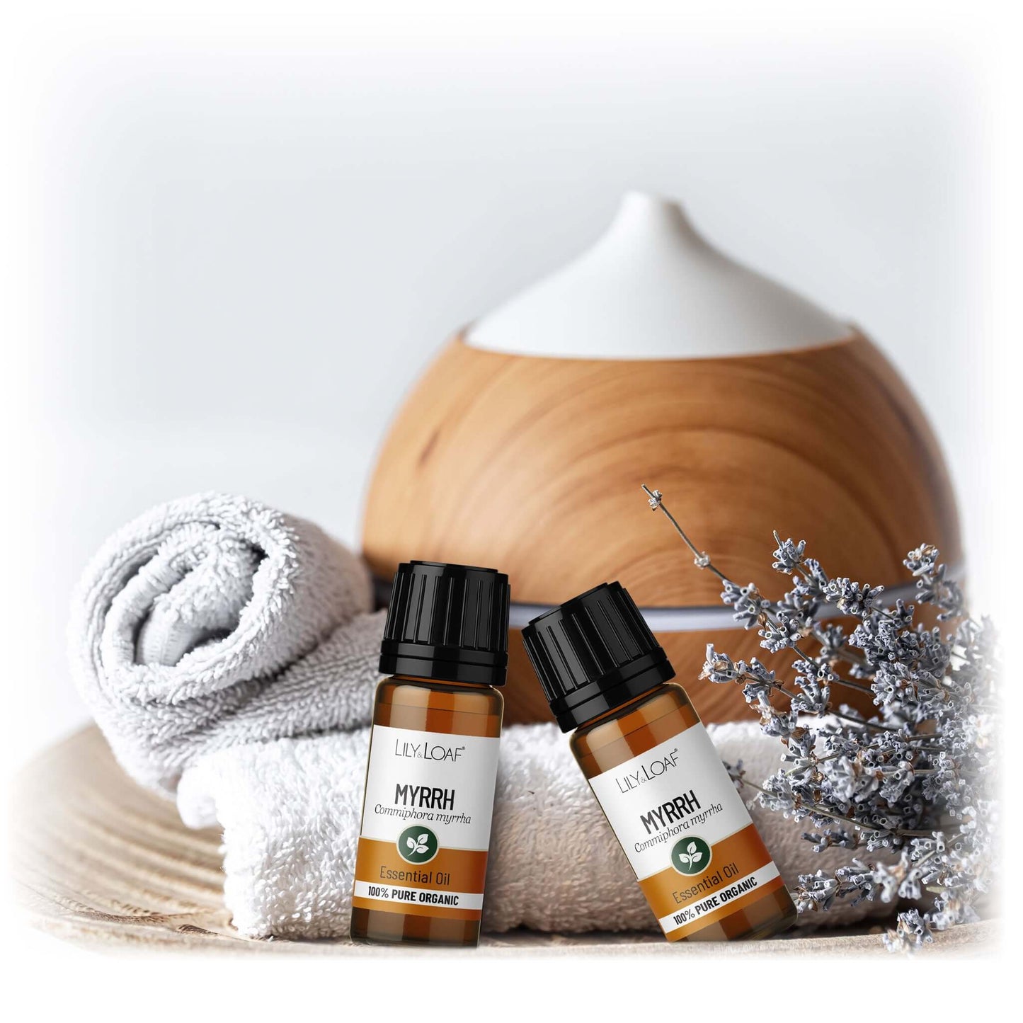 Two bottles of Lily & Loaf Myrrh essential oil with a diffuser and towel on a light background