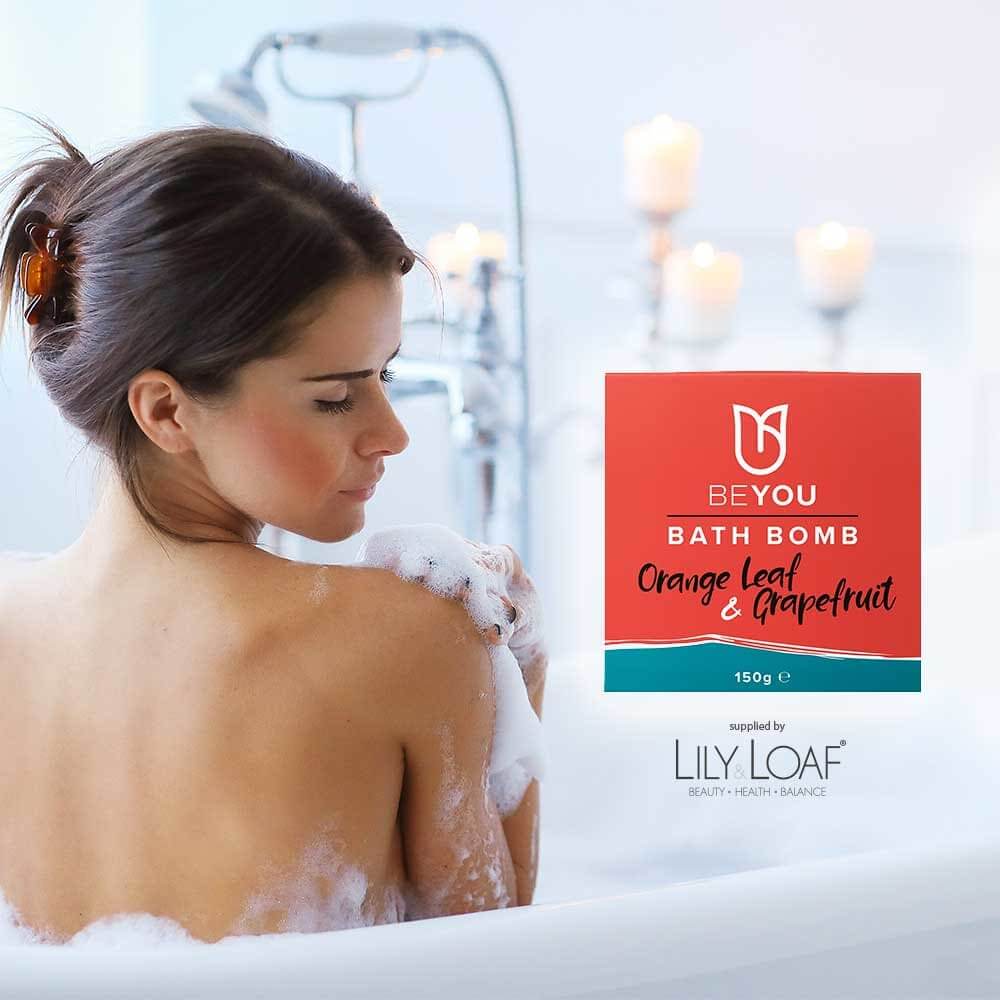 A woman in the bath with the BeYou Orange Leaf & Grapefruit Bath Bomb in the foreground