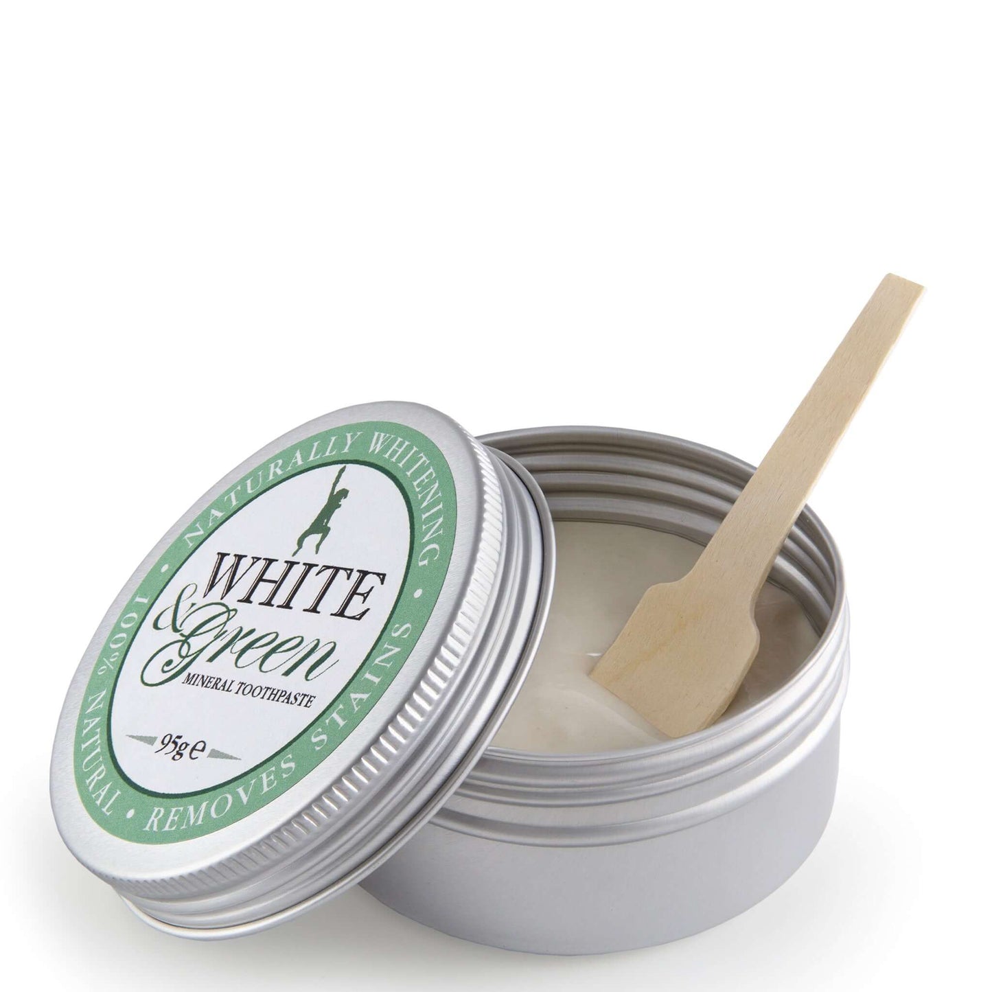 Open tin of White & Green mineral toothpaste with silver lid, green label, and wooden spatula resting inside the creamy paste