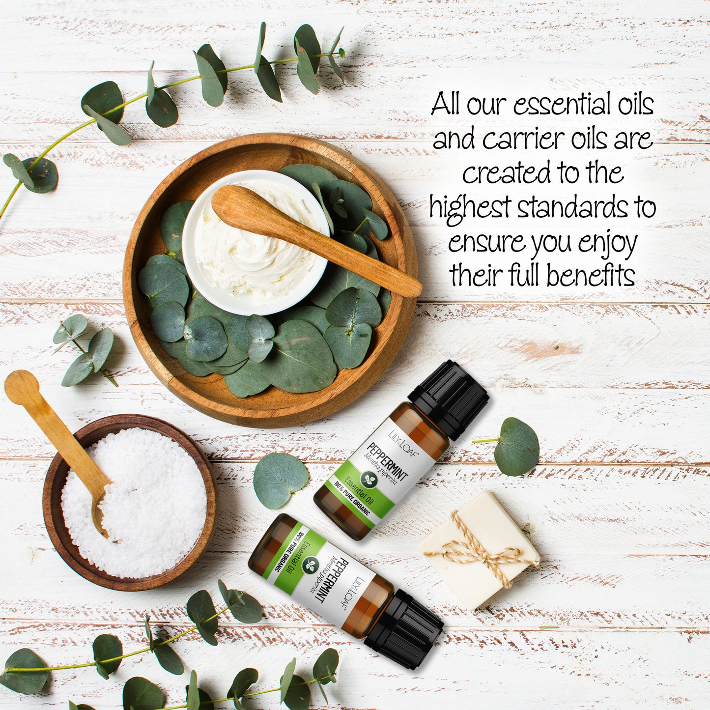 Peppermint essential oil bottles displayed with eucalyptus leaves, bath salt, and cream on a white wooden background. Highlights the high quality of Lily & Loaf's essential and carrier oils.