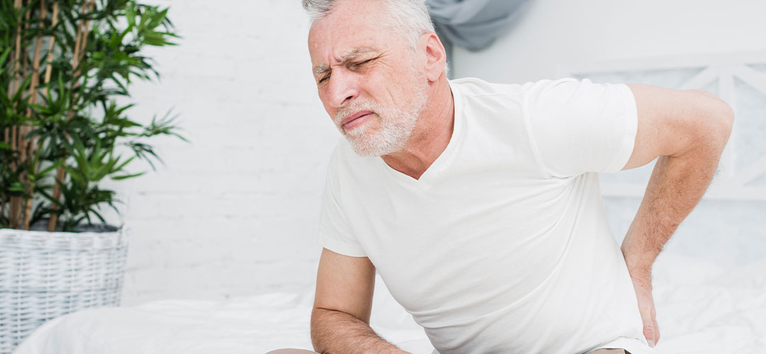 Older man holding his lower back in pain, highlighting the need for holistic approaches to managing chronic pain and improving quality of life