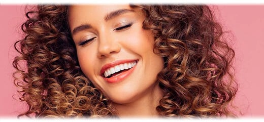A woman with curly brown hair, smiling with perfect white teeth