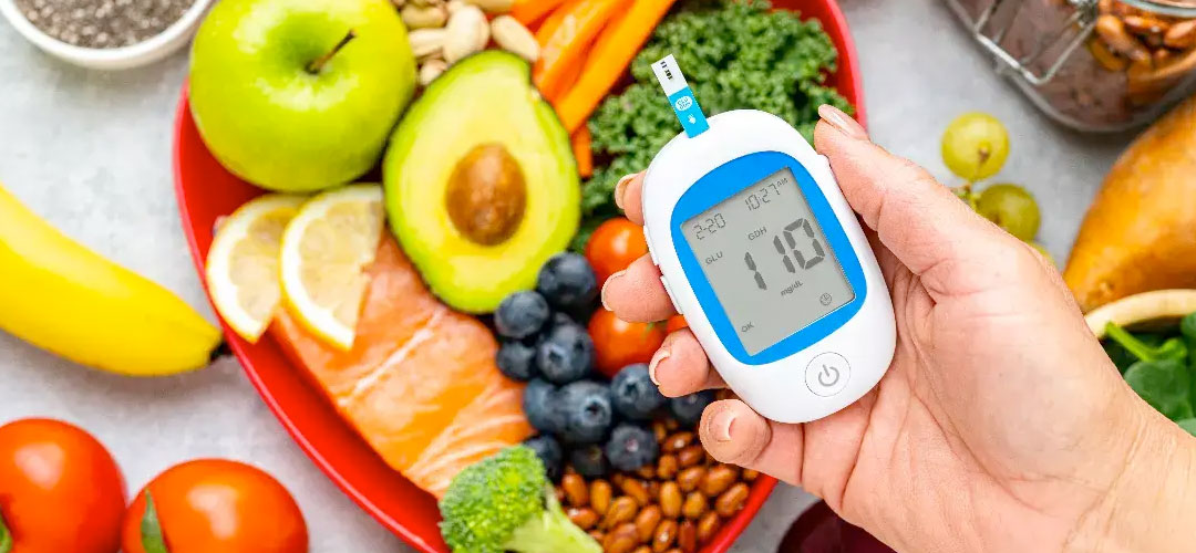 Hand holding glucose meter near healthy foods like avocado, berries, salmon and vegetables