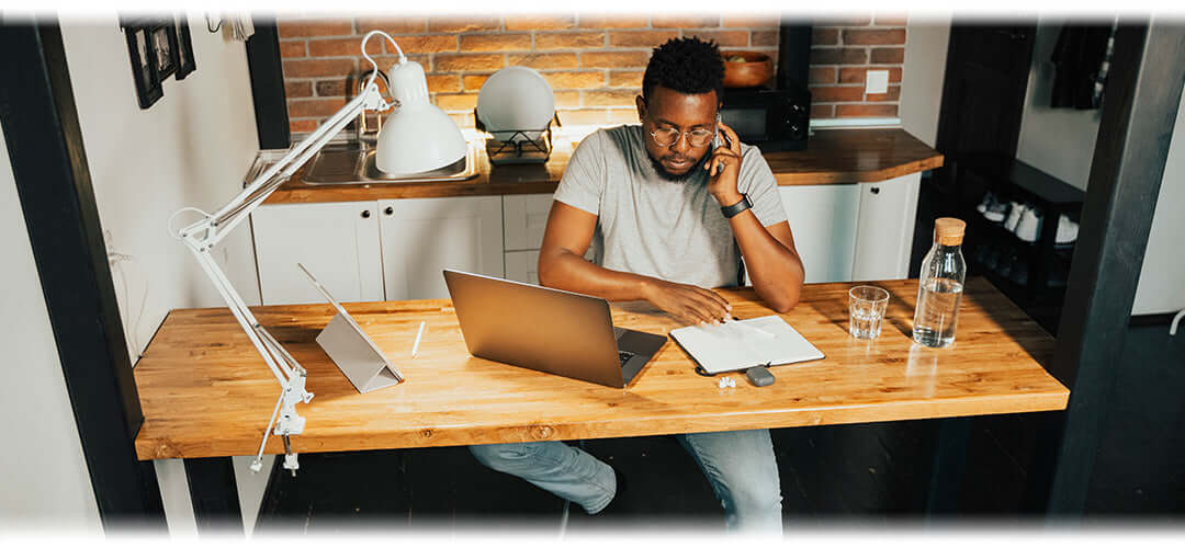 A person working on a laptop at a home office setup with a cup of tea and healthy snacks nearby.