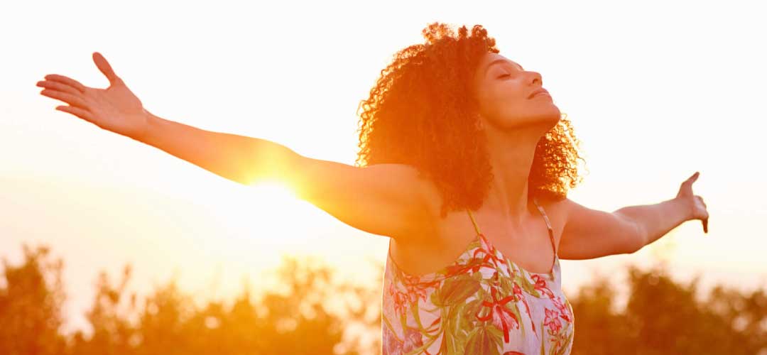 Joyful woman embracing the sunshine with arms outstretched in a summer dress.