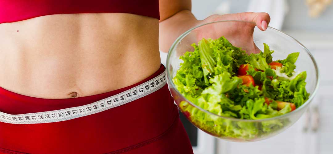 female holding salad bowl with tape measure around her waist