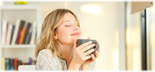 A blonde woman smiling whilst enjoying a hot beverage