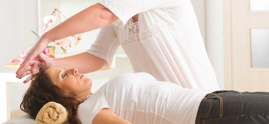 Practitioner performing Reiki energy healing above relaxed woman lying on therapy table
