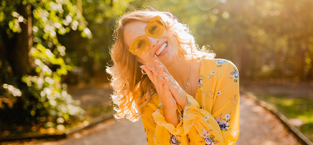 Smiling woman in sunlight wearing yellow, symbolising the vibrant benefits of vitamin C for immune support, skin health, and overall wellness