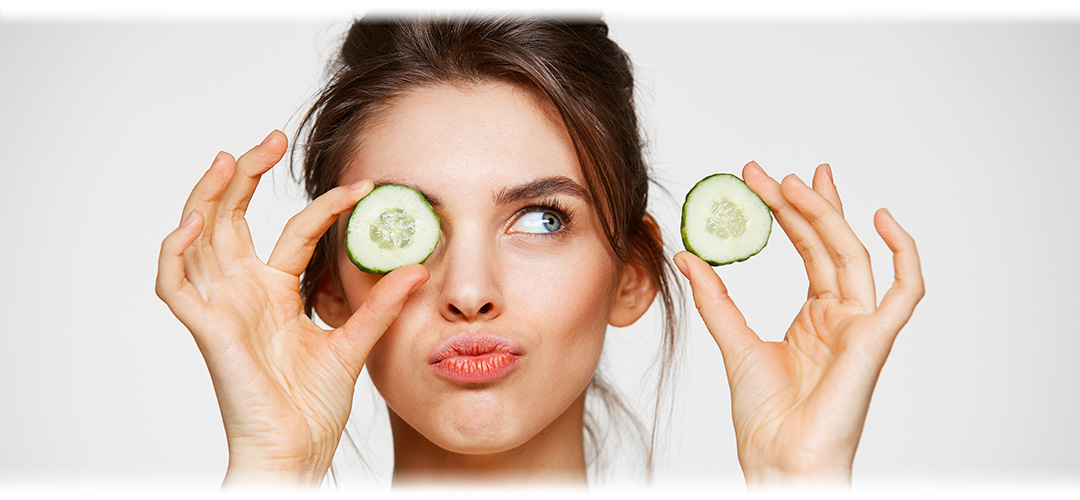A woman holding cucumbers against her eyes