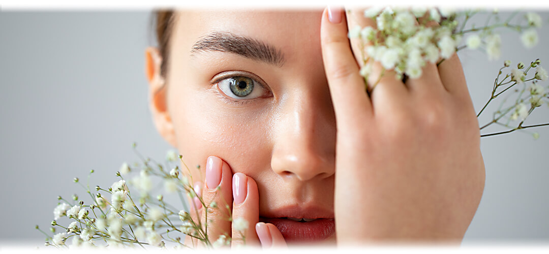 A close up of a woman's face, she is holding flowers against her skin