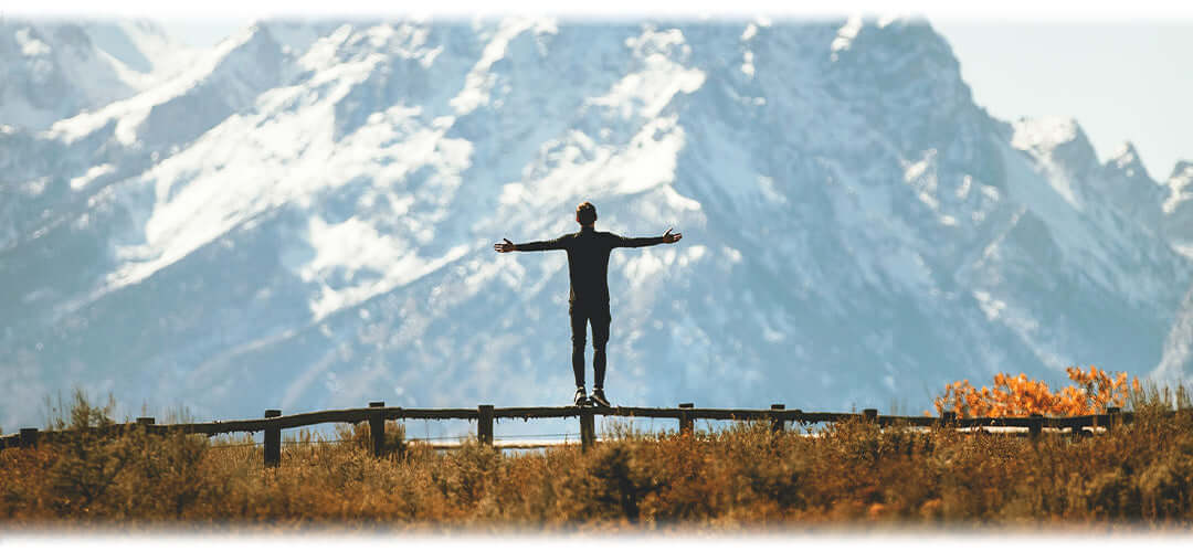 A person stood looking at a mountain range with their arms outstretched in joy