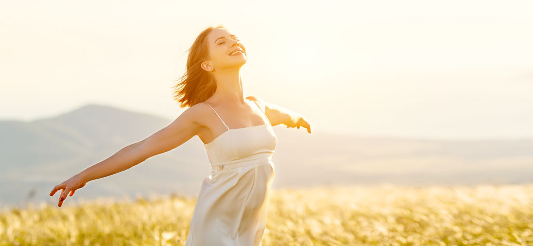 Happy woman enjoying sunlight in a meadow, symbolising the rejuvenating benefits of spring detox for improved energy and overall health