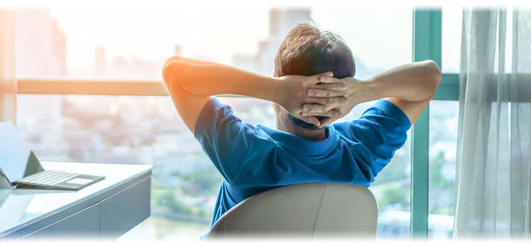 A man sat in a glass window office relaxing looking out at the view