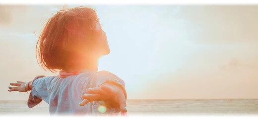 A woman at the beach with her arms outstretched enjoying the sunset