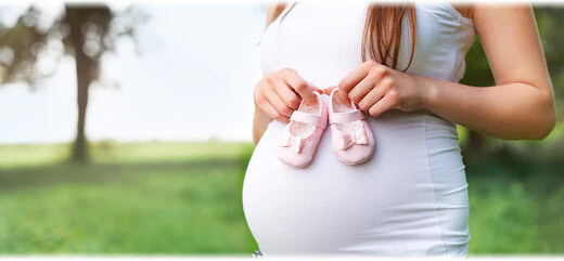 A pregnant woman holding pink baby booties against her belly