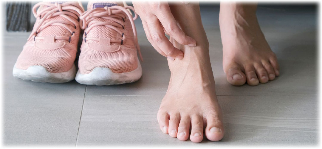 A person massaging their sore foot beside a pair of pink athletic shoes
