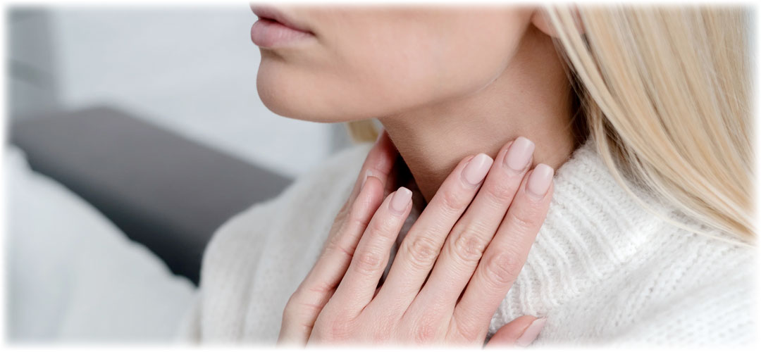 Close-up of a woman with blonde hair touching her throat, wearing a white sweater.