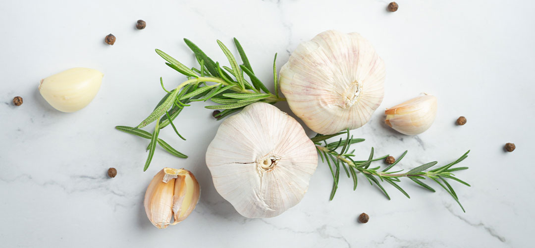Garlic bulbs, rosemary sprigs, and peppercorns on a marble surface, highlighting natural herbal remedies for treating common ailments