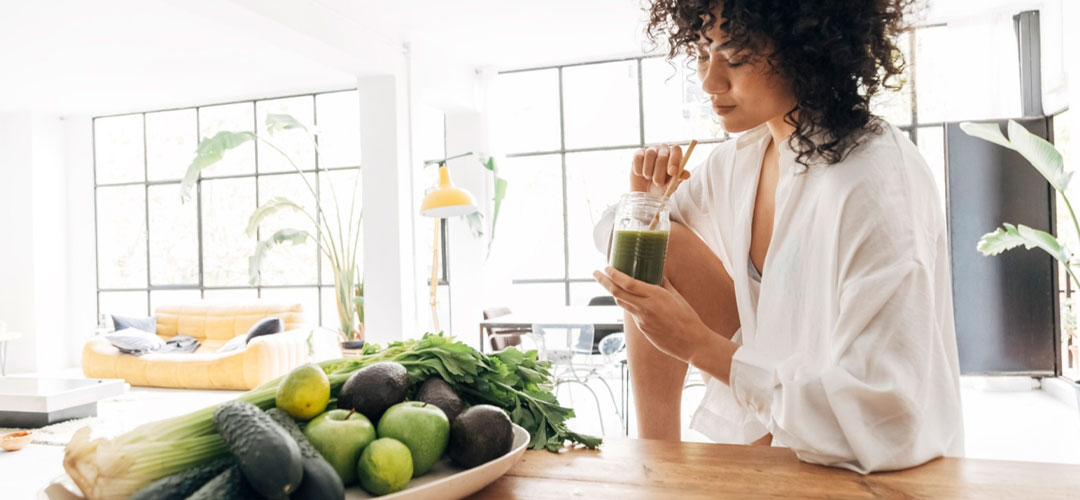 Woman drinking a green smoothie near fresh vegetables, highlighting the health benefits of chlorophyll for detoxification and overall wellness