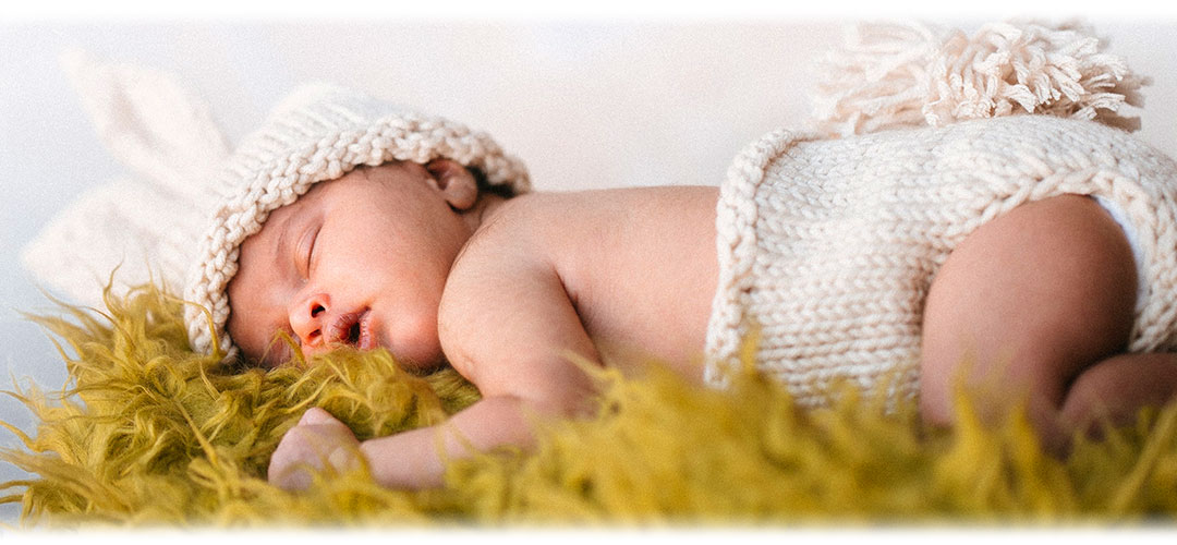A sleeping new born baby wearing a white bonnet with bunny ears