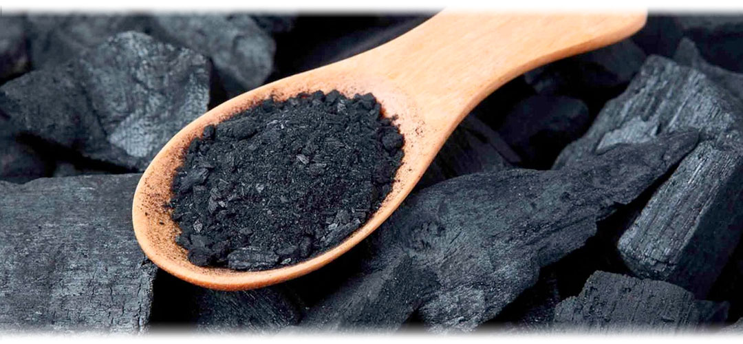 A wooden spoon containing charcoal on a bed of larger charcoal pieces