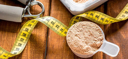 A scoop of protein powder surrounded by exercise items and a tape measure