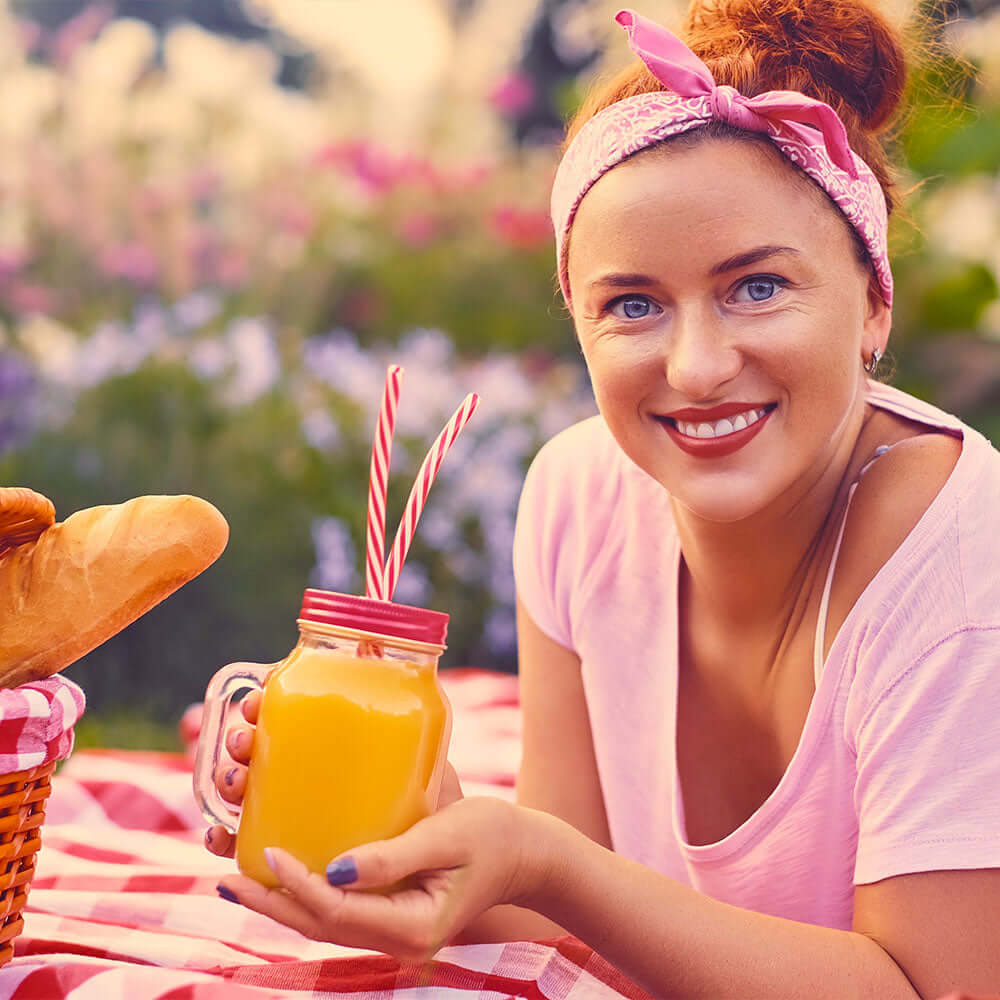 Woman smiling holding an orange juice at a picnic, representing a healthy daily nutrition routine