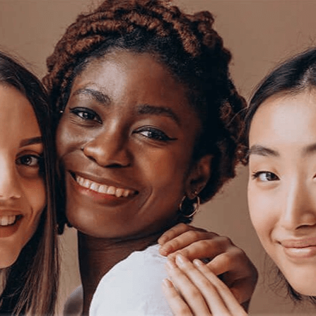 Three smiling women standing close together, showcasing healthy, glowing skin.