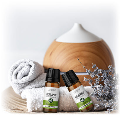 Lily & Loaf Organic Bergamot Essential Oil bottles with a diffuser, rolled towel, and dried flowers, creating a calming and aromatic spa-like setting.