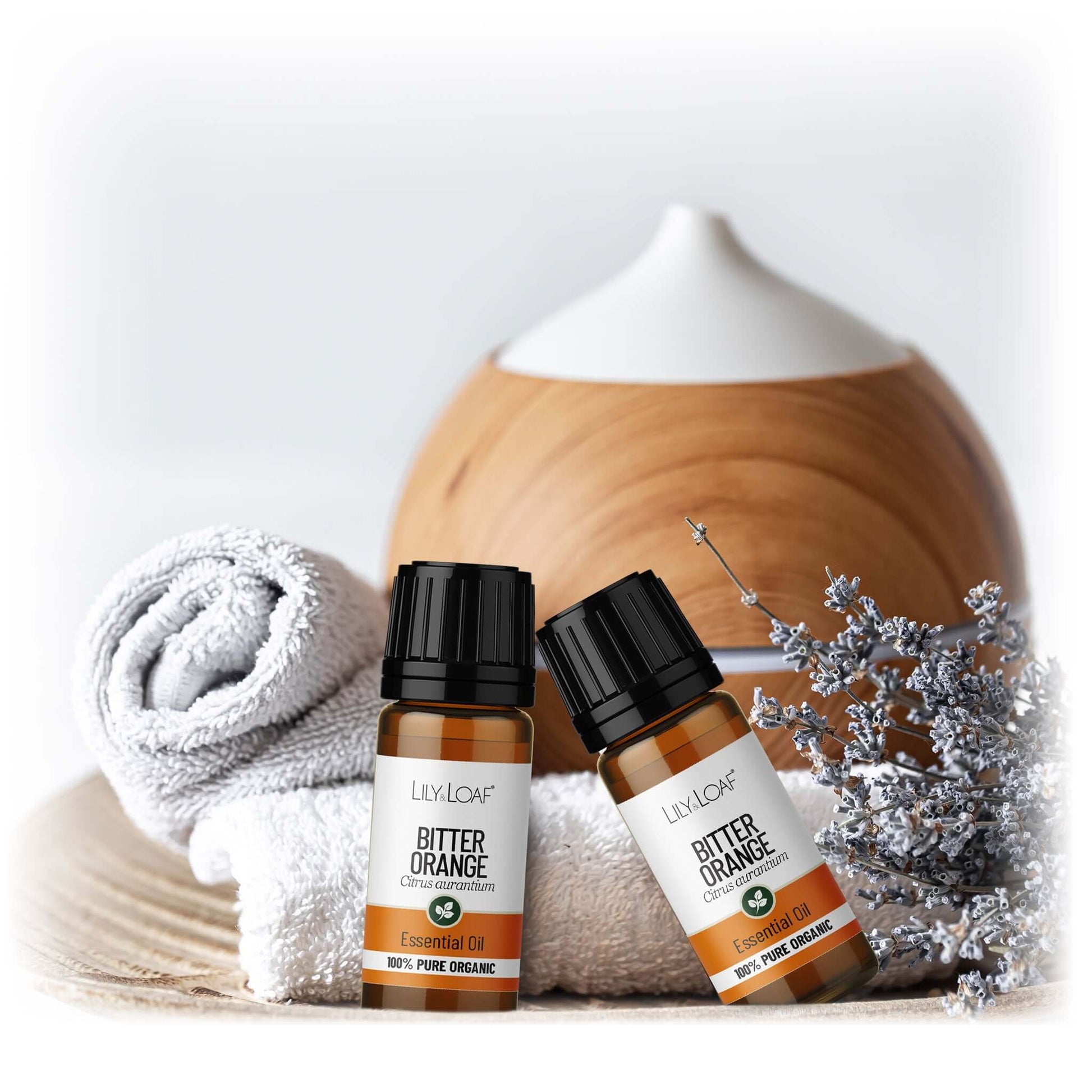 Two bottles of Lily & Loaf Bitter Orange essential oil with a diffuser and towel in the background.