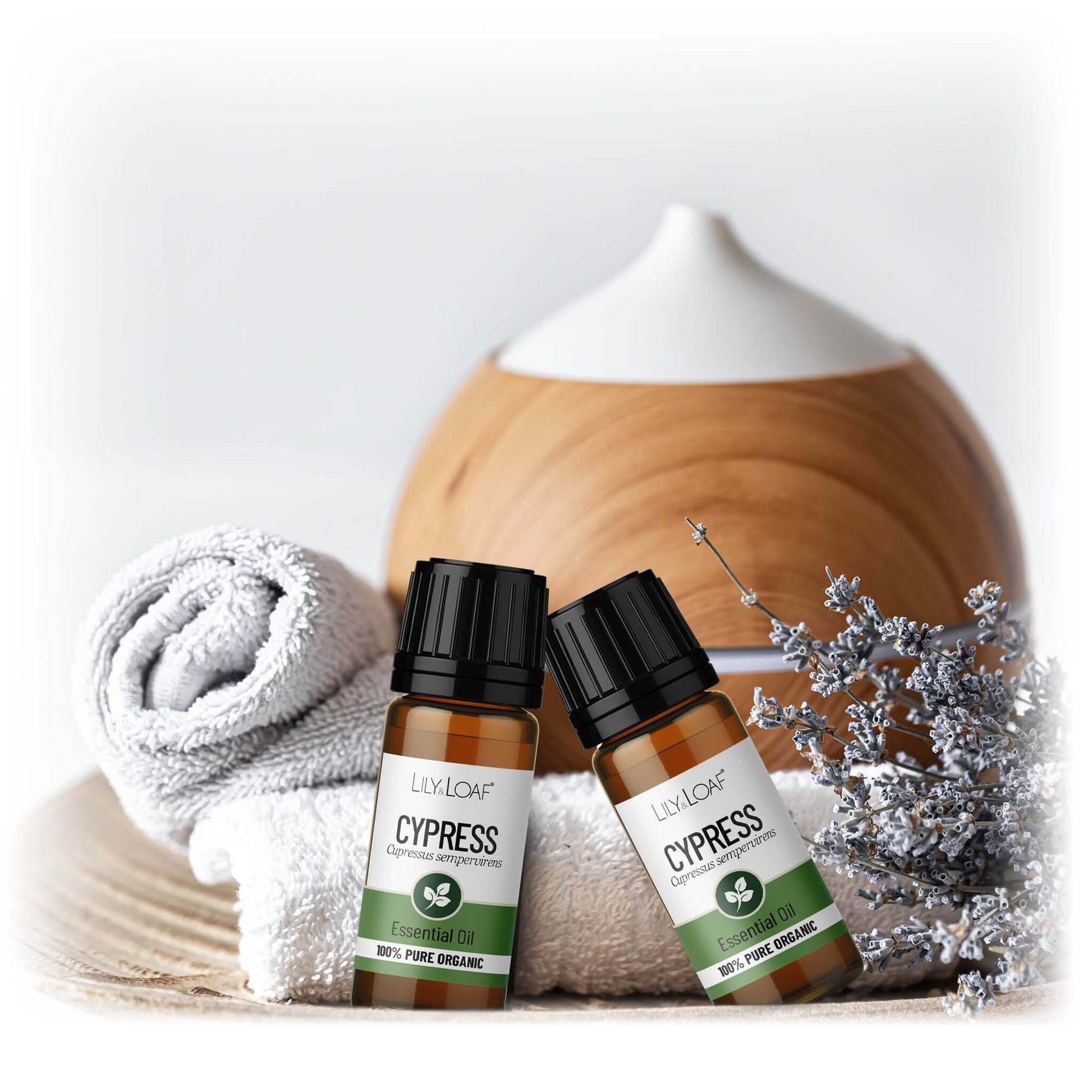 Two bottles of Cypress essential oil with a wooden diffuser and decorative elements on a light background