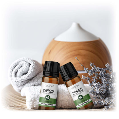 Two bottles of Cypress essential oil with a wooden diffuser and decorative elements on a light background