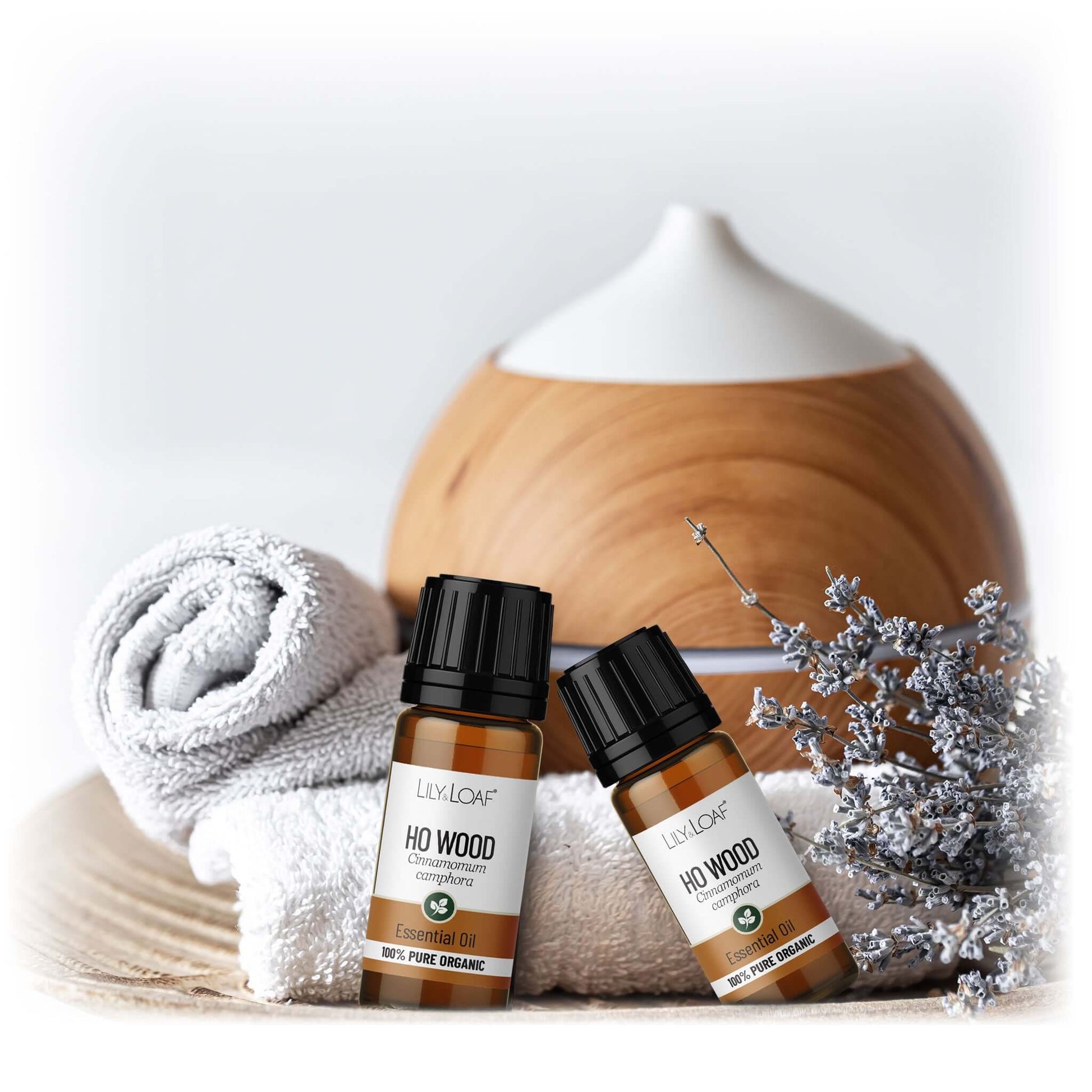 Two bottles of 'Ho Wood' essential oil with a diffuser and towel on a light background