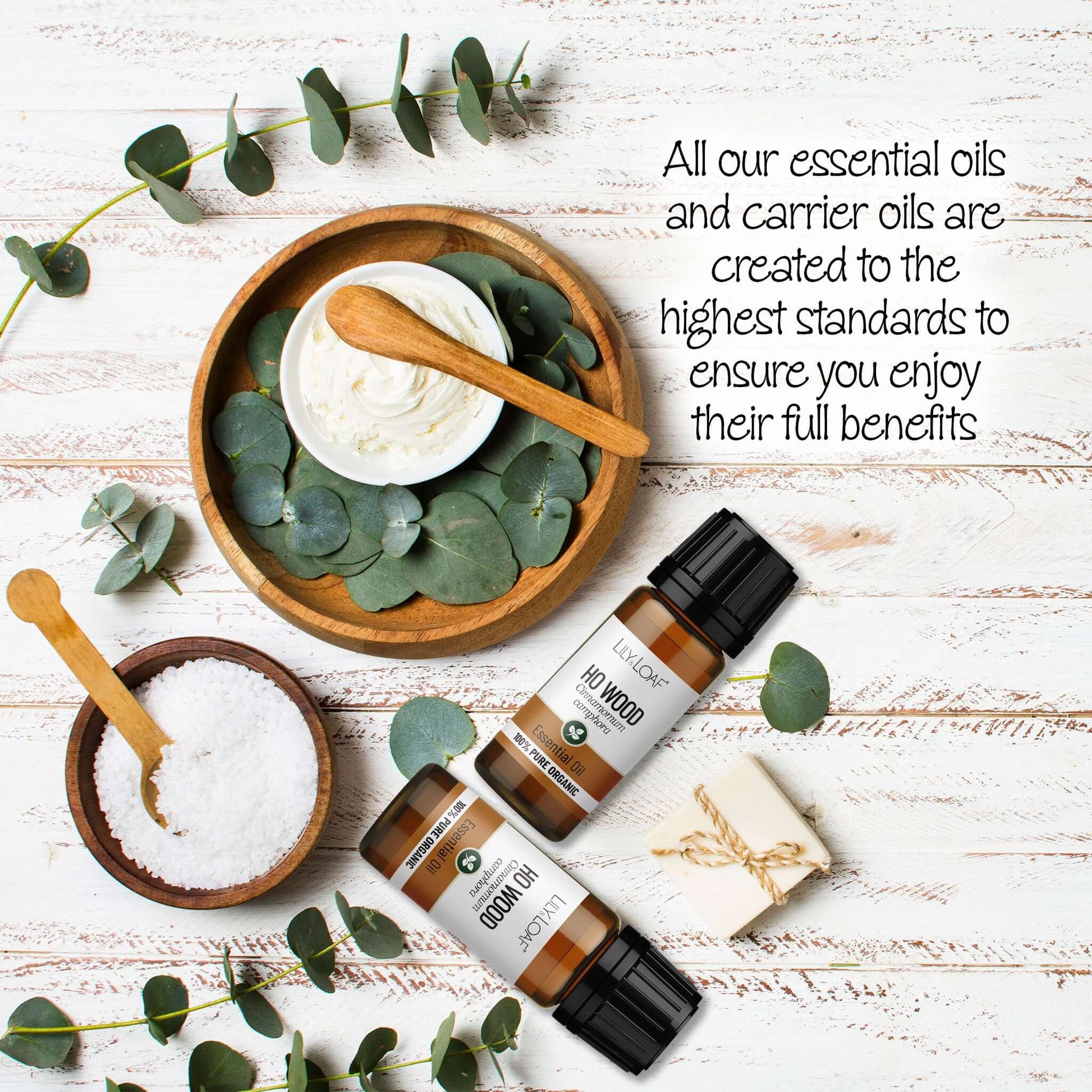 Ho Wood Essential Oil surrounded by eucalyptus leaves and wooden bowls on a wooden surface