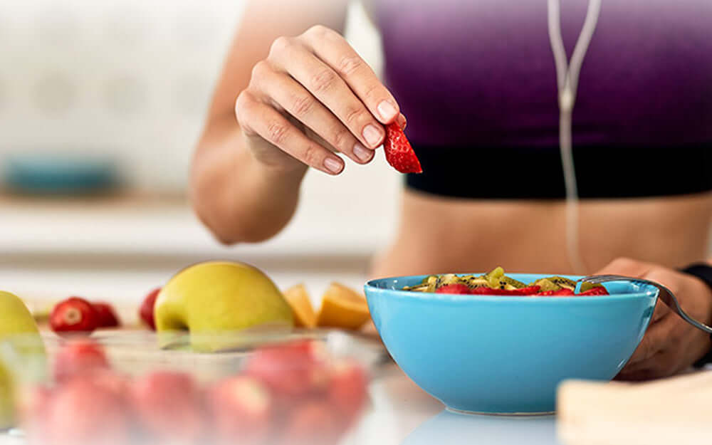 A woman preparing a smoothie bowl with healthy digestive system foods such as apples and strawberries