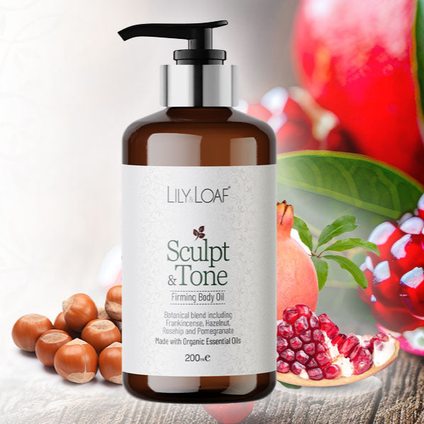 Bottle of Lily & Loaf Sculpt & Tone Firming Body Oil with pomegranate and hazelnut elements in the background