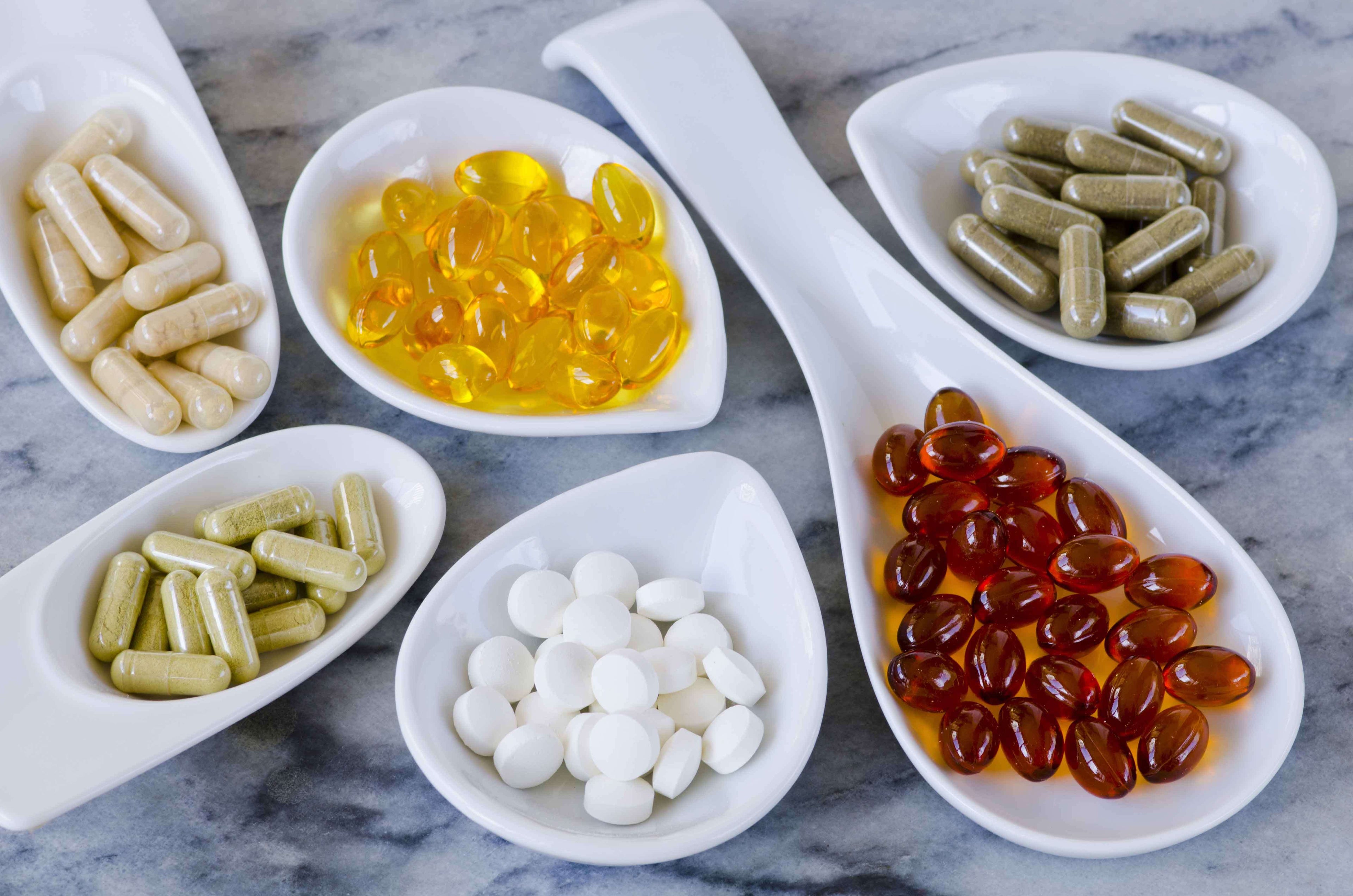 A range of different coloured capsules and tablets in spoons and bowls