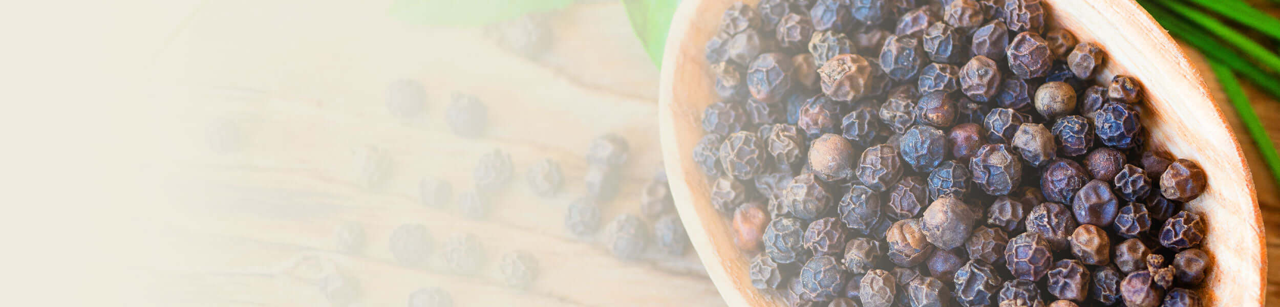 A wooden bowl filled with whole black peppercorns, highlighting the spice used to create Black Pepper essential oil.