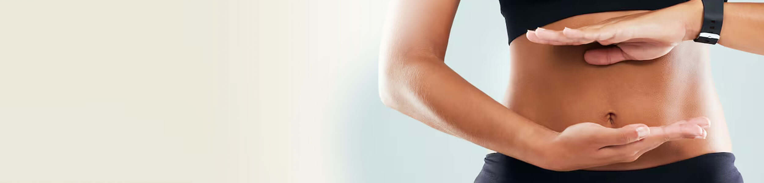 A healthy, toned woman wearing black gym wear holding her hands against her stomach in a harmony sign 