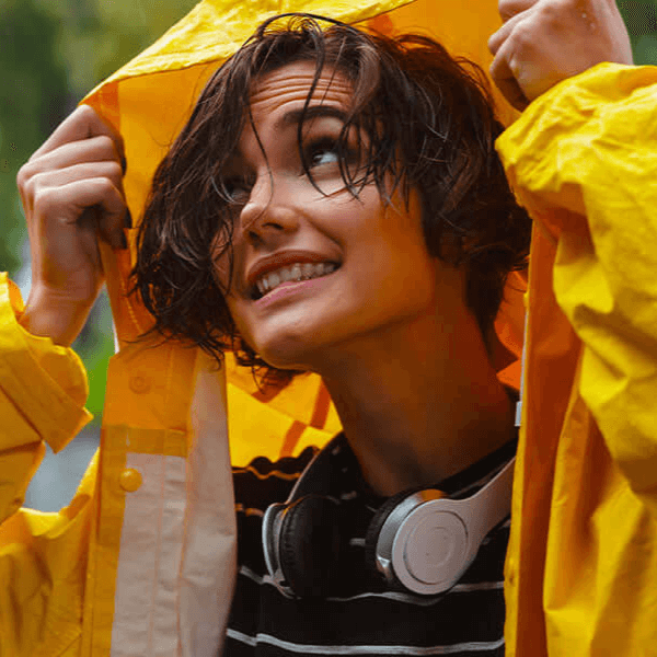 Smiling woman in a yellow raincoat with wet hair, symbolising resilience and the importance of a strong immune system for overall well-being