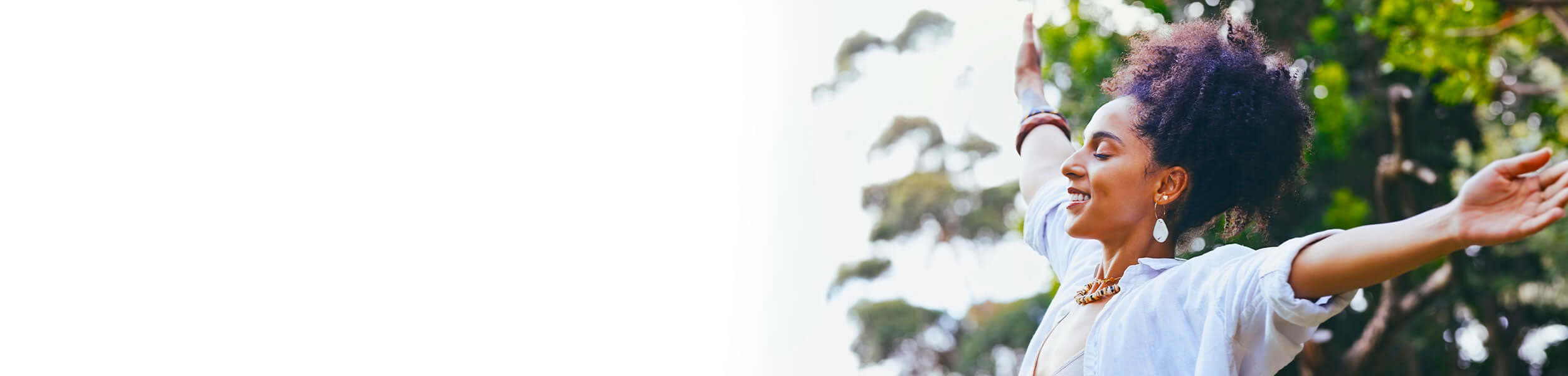 Smiling woman with arms outstretched in nature, embracing a sense of wellbeing and balance.