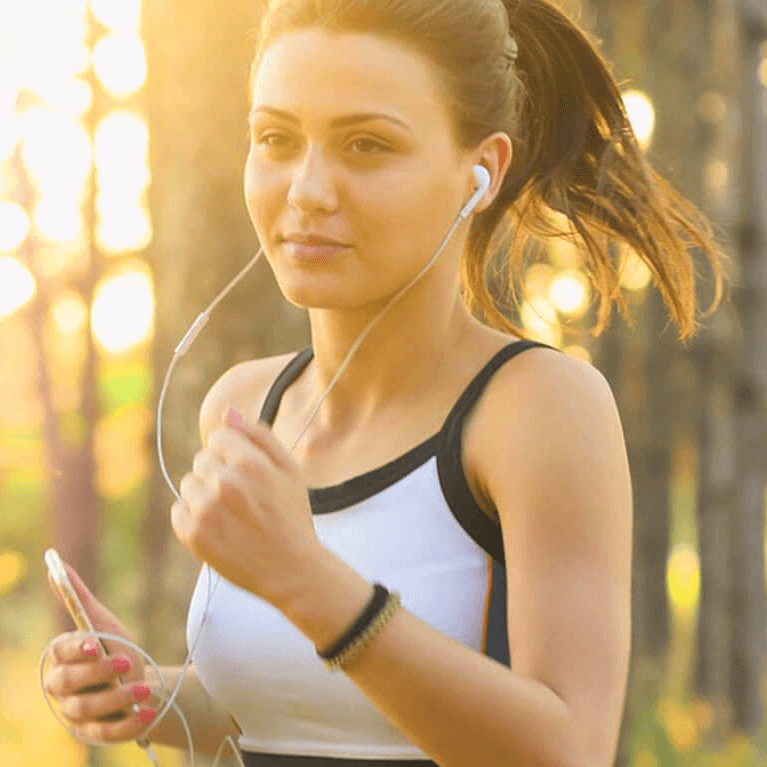 Young woman jogging outdoors with earphones, representing the importance of sports, fitness, and active living for a healthy lifestyle