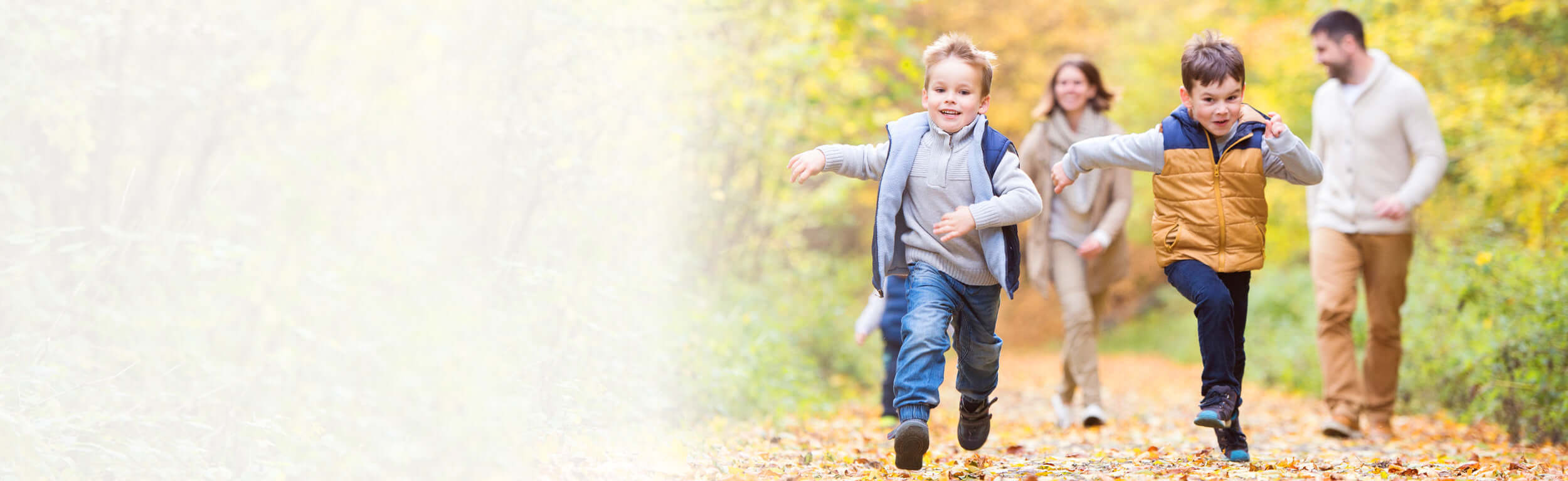 A family of mum, dad and two boys who are running through an autumn forest