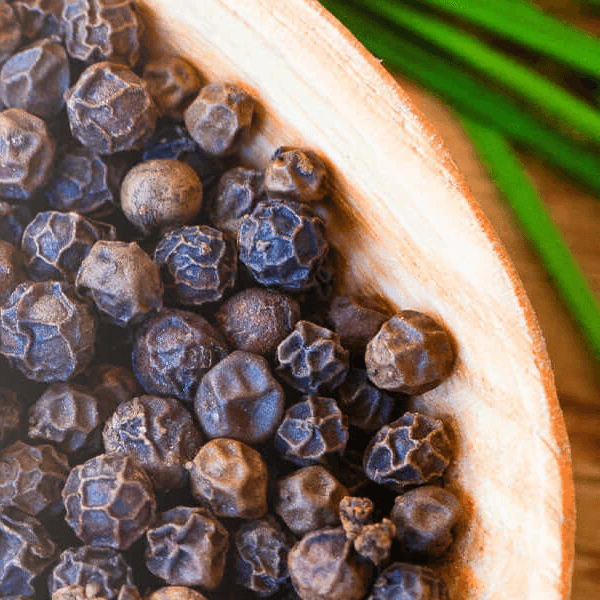Whole black peppercorns in a wooden bowl with green herb garnish