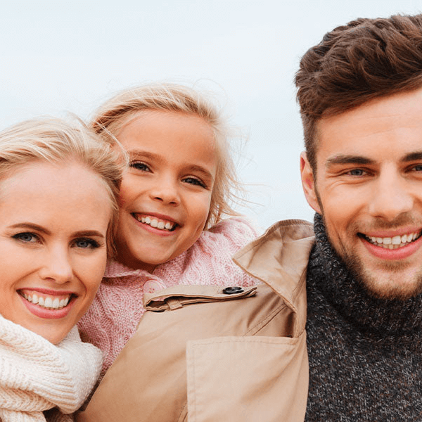 A family of three smiling and wearing winter clothes whilst out for a walk