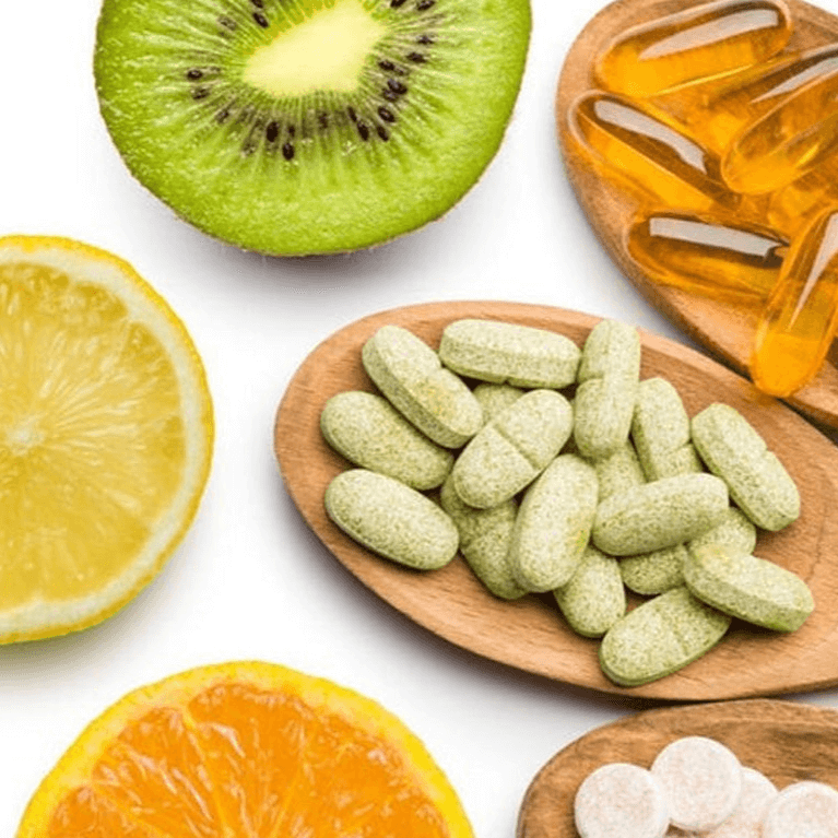 Fresh citrus fruits, kiwi, and supplement tablets on wooden spoons, symbolising a comprehensive guide to essential vitamins for health and wellness