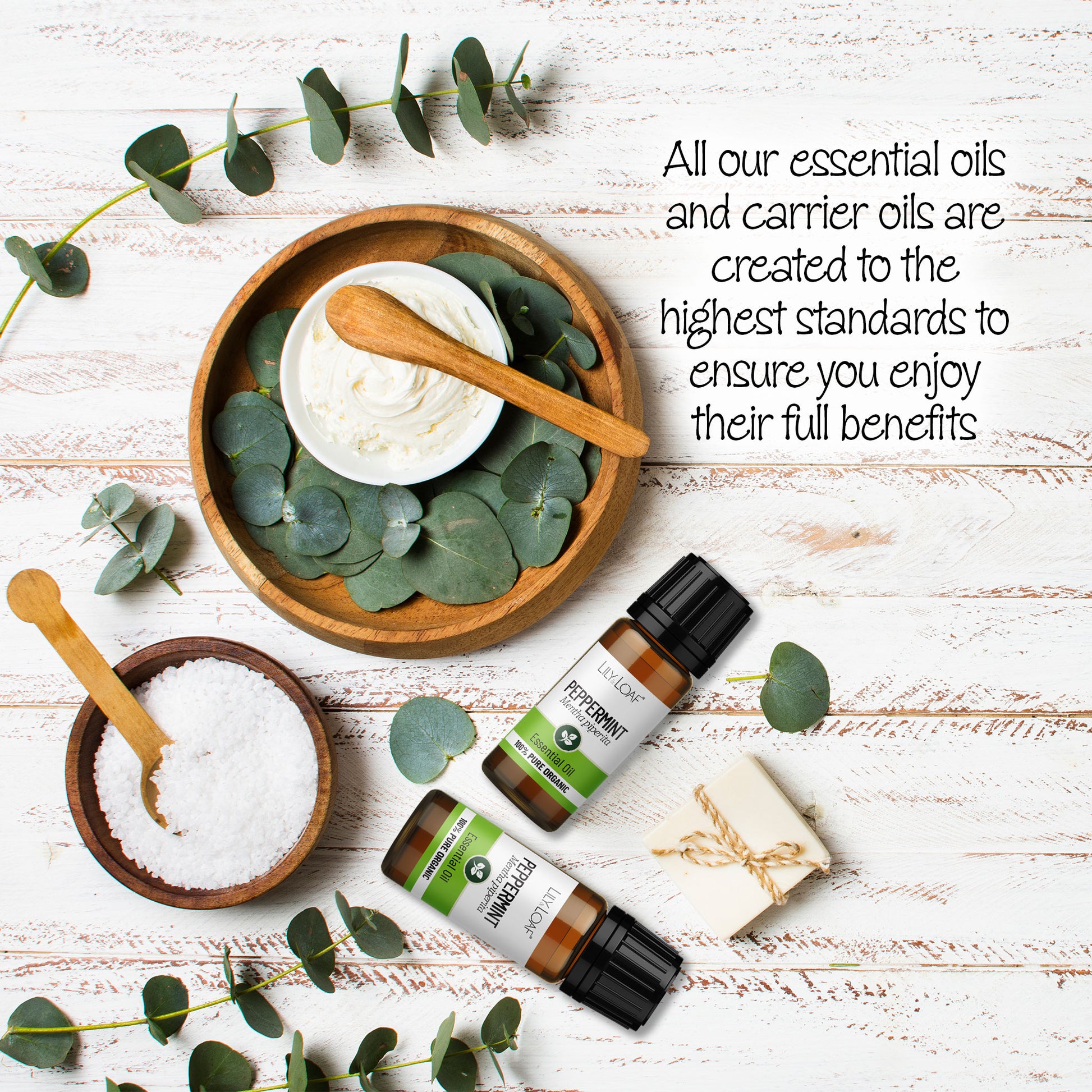 Peppermint essential oil bottles displayed with eucalyptus leaves, bath salt, and cream on a white wooden background. Highlights the high quality of Lily & Loaf's essential and carrier oils.